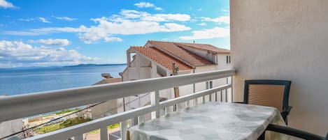 Een balkon met een tafel en stoelen, met uitzicht op een kustgebied met gebouwen en een heldere lucht.