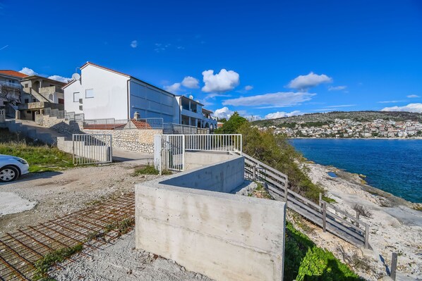 Ein Küstengebäude mit weißer Fassade, einer Steintreppe und Blick auf das Meer und die Stadt im Hintergrund.
