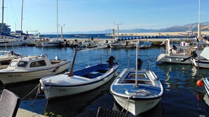 A marina with several boats docked, a lighthouse in the background, and a clear view of the sea and distant mountains. - Apartments Mare (Postira)