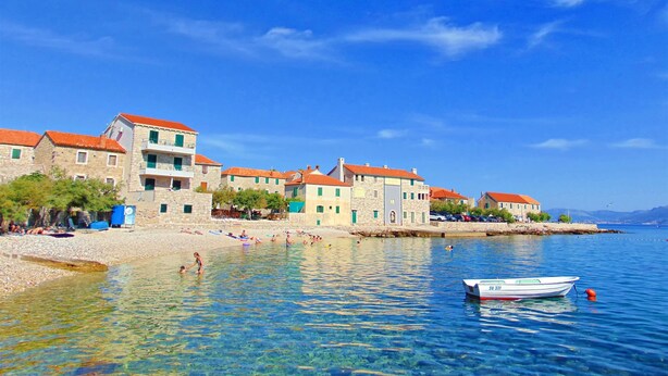 A coastal town with stone buildings, clear waters, and a boat docked near the shore. - Apartments Mare (Postira)