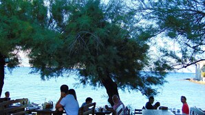 A lakeside restaurant with outdoor seating, wooden tables, and benches, surrounded by trees. - Apartments Mare (Postira)