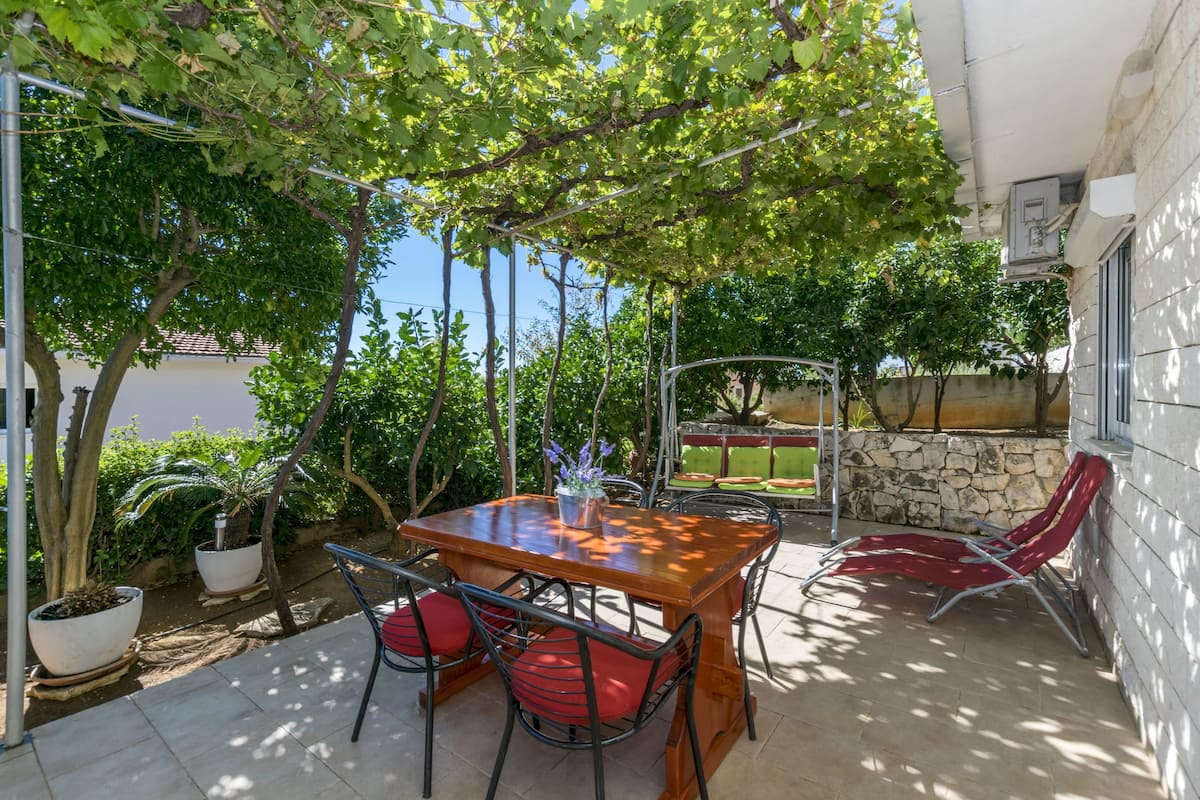 Eine Terrasse mit Holztisch und roten Stühlen, umgeben von Blumentöpfen und einer Steinmauer.