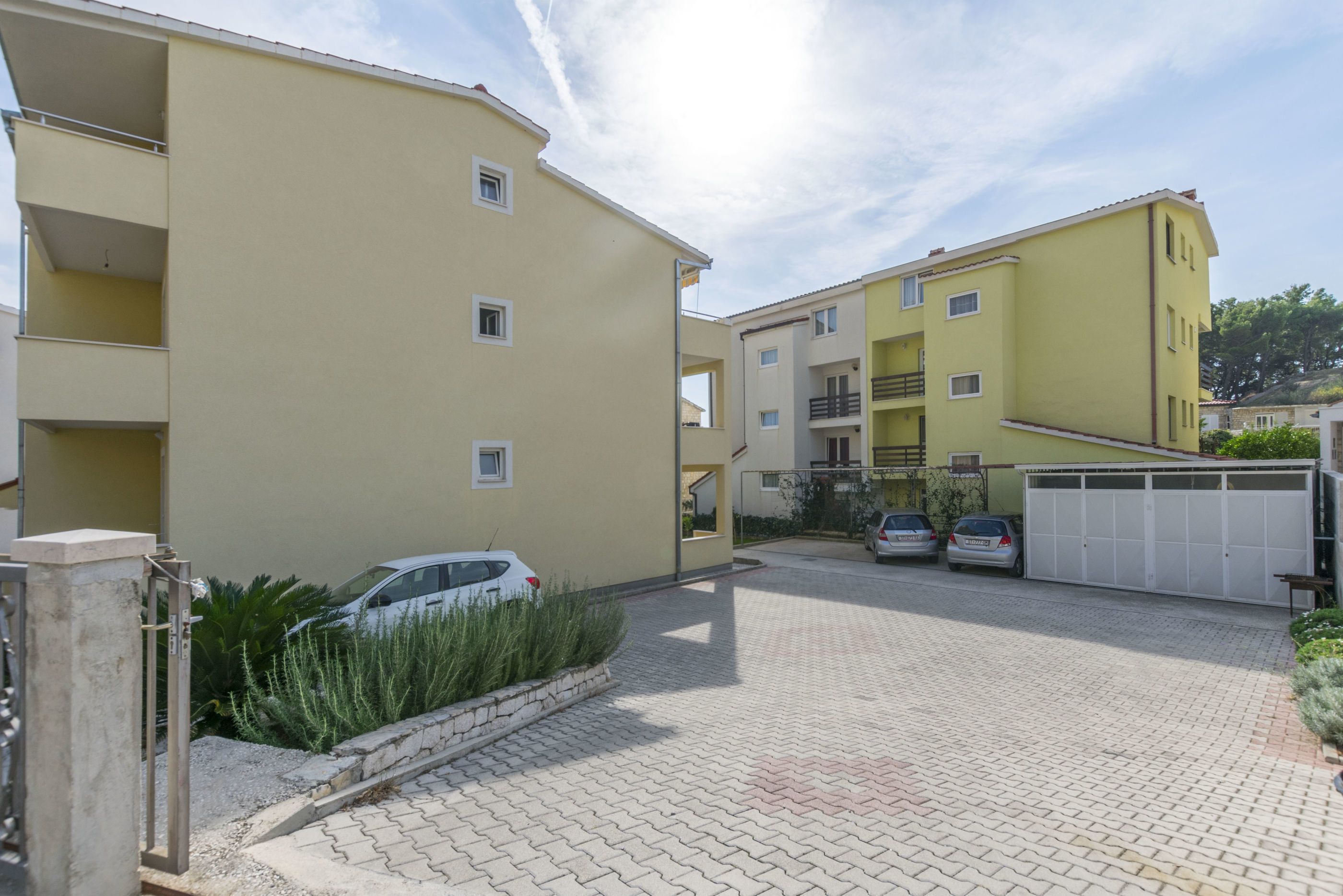 A residential building with a paved driveway, a gated entrance, and parked cars.