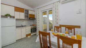 A modern kitchen with white cabinets, a dining table set with orange juice, and a view through the window. - Apartments Srecko (Duce)