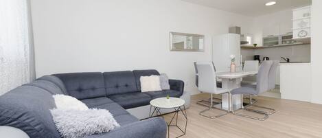 Una sala de estar moderna con un sofá seccional gris, una mesa de centro redonda y una zona de comedor con una mesa y sillas blancas.