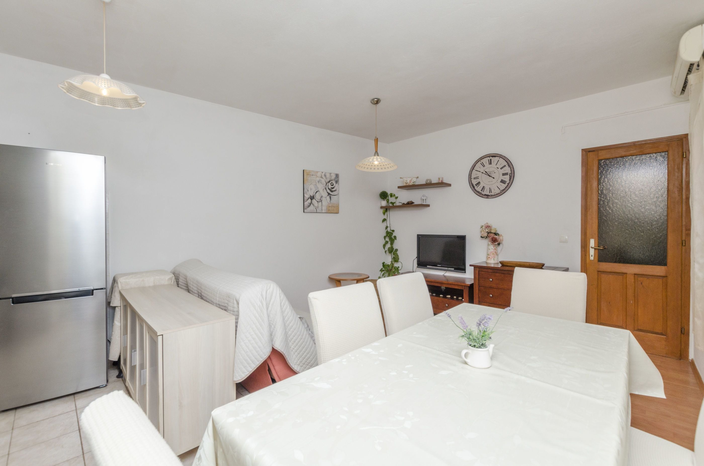 A compact living space with a kitchenette, a dining area with a table and chairs, a TV, and a door with frosted glass.