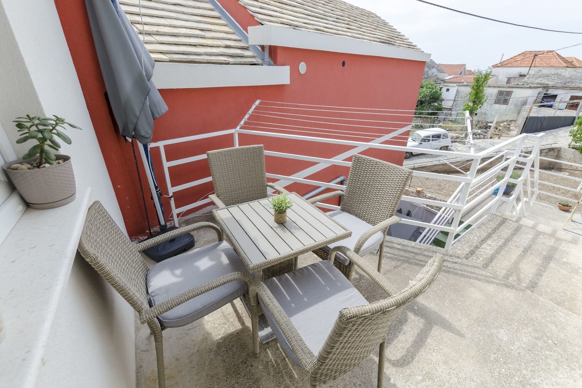 A balcony with wicker furniture, a small table with a plant, and a red wall.