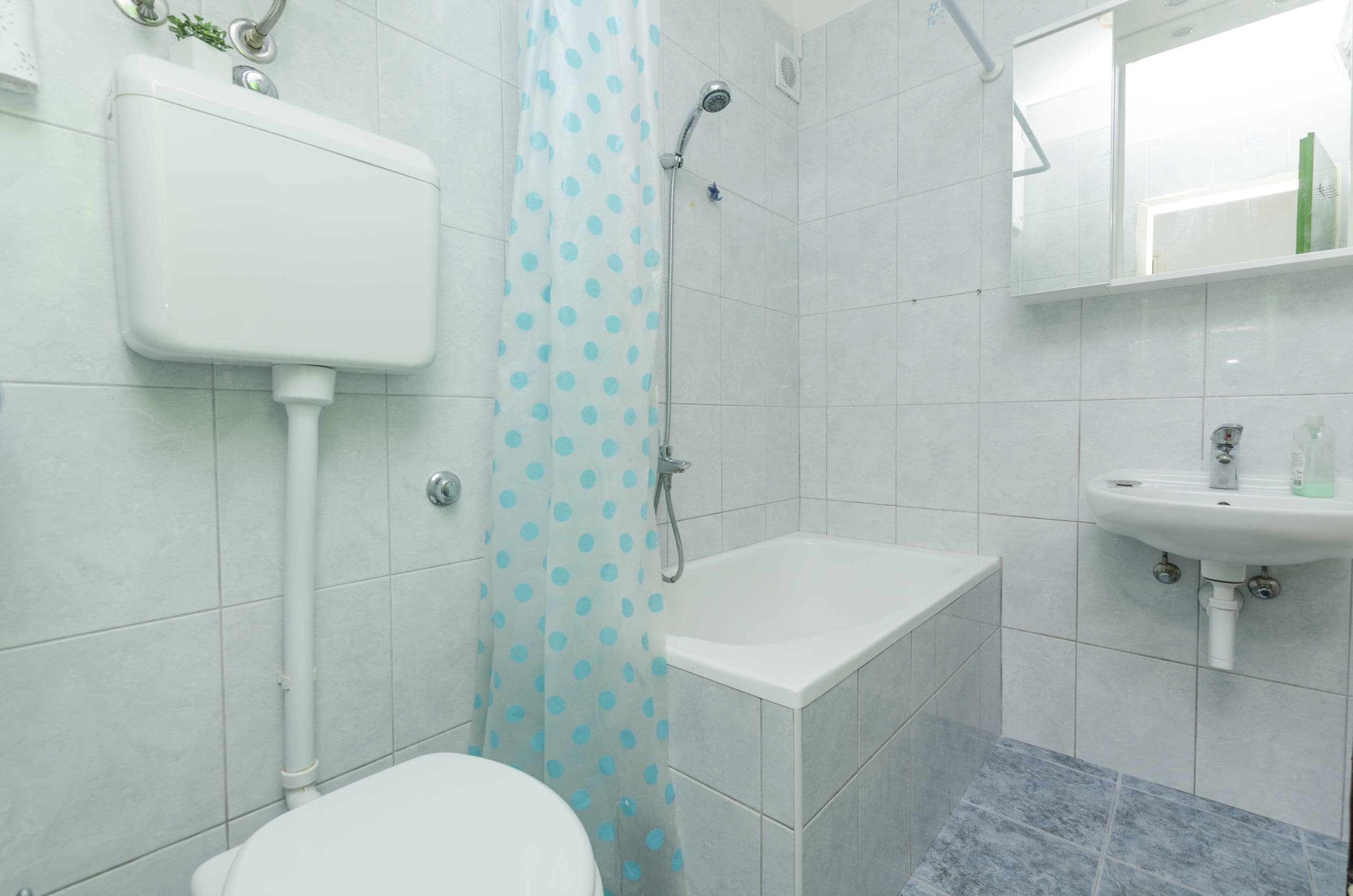 A bathroom with a toilet, a shower with a polka dot curtain, a bathtub, and a sink with a mirror above it.