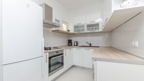 Una cuina moderna amb armaris blancs, forn integrat, cafetera i un rellotge a la paret.