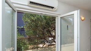 A room with a sliding glass door leading to an outdoor area, a white air conditioning unit above the door, and a wall-mounted light fixture. - Apartment Ljuba (Primosten)