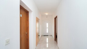 A narrow, well-lit hallway with wooden doors and a tiled floor, leading to a bright room. - Apartment Ljuba (Primosten)