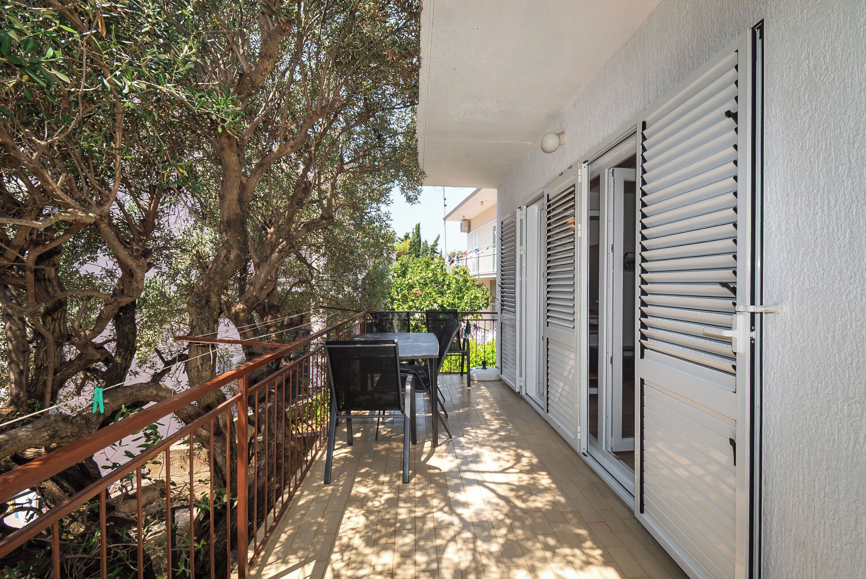 A balcony with a table and chairs, a railing, and a view of trees and buildings.