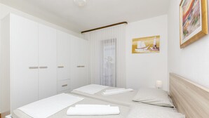 A hotel room with a bed, a nightstand, a window with curtains, and a painting on the wall. - Apartments Denis (Supetar)