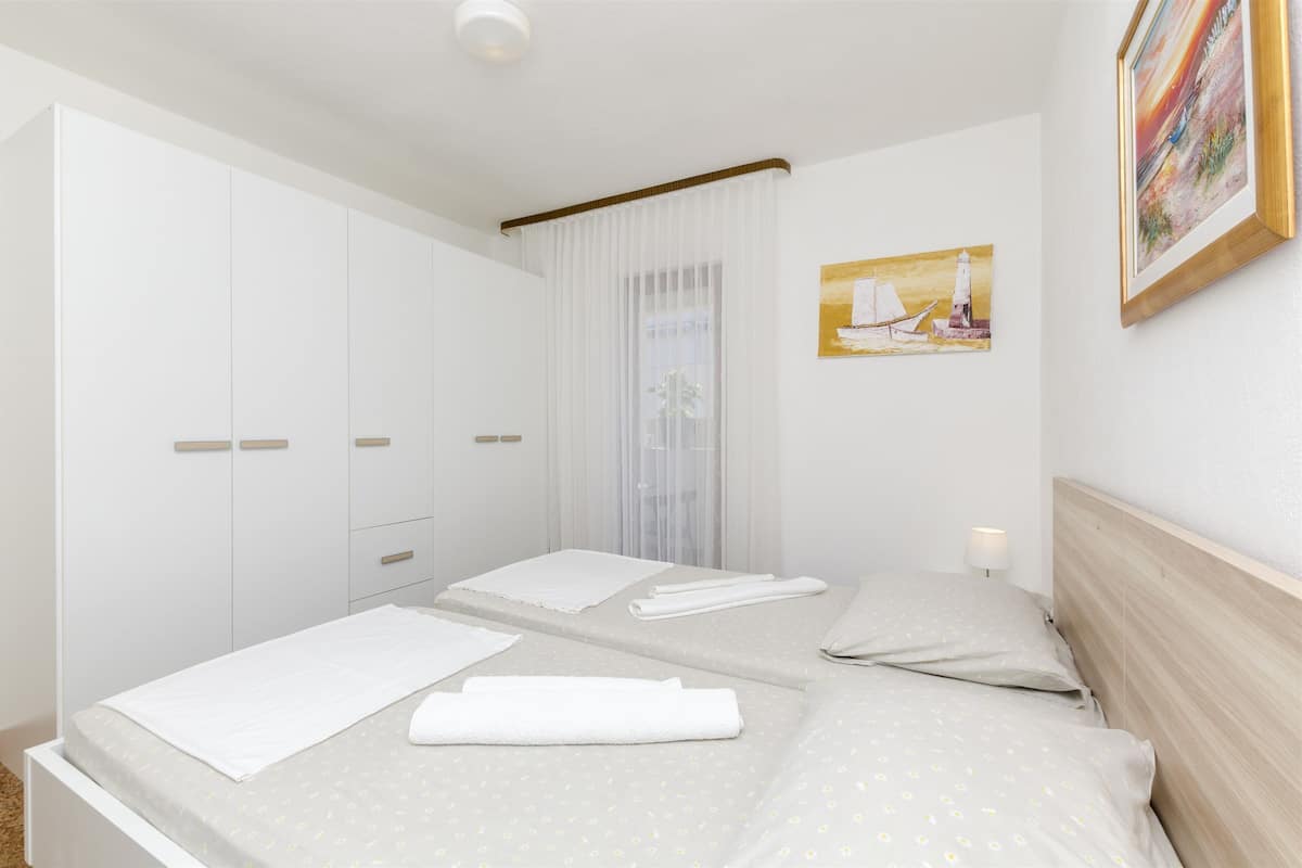 A hotel room with a bed, a nightstand, a window with curtains, and a painting on the wall.