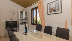 A dining area with a table, chairs, a television, a cabinet, and a window with curtains. - Apartments Denis (Supetar)