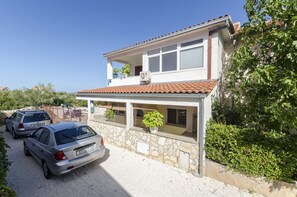 A two-story house with a stone facade, a tiled roof, and a balcony. There are two cars parked in front. - Apartments Denis (Supetar)