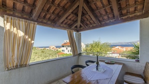 A balcony with a wooden table, chairs, and a bench. - Apartments Denis (Supetar)