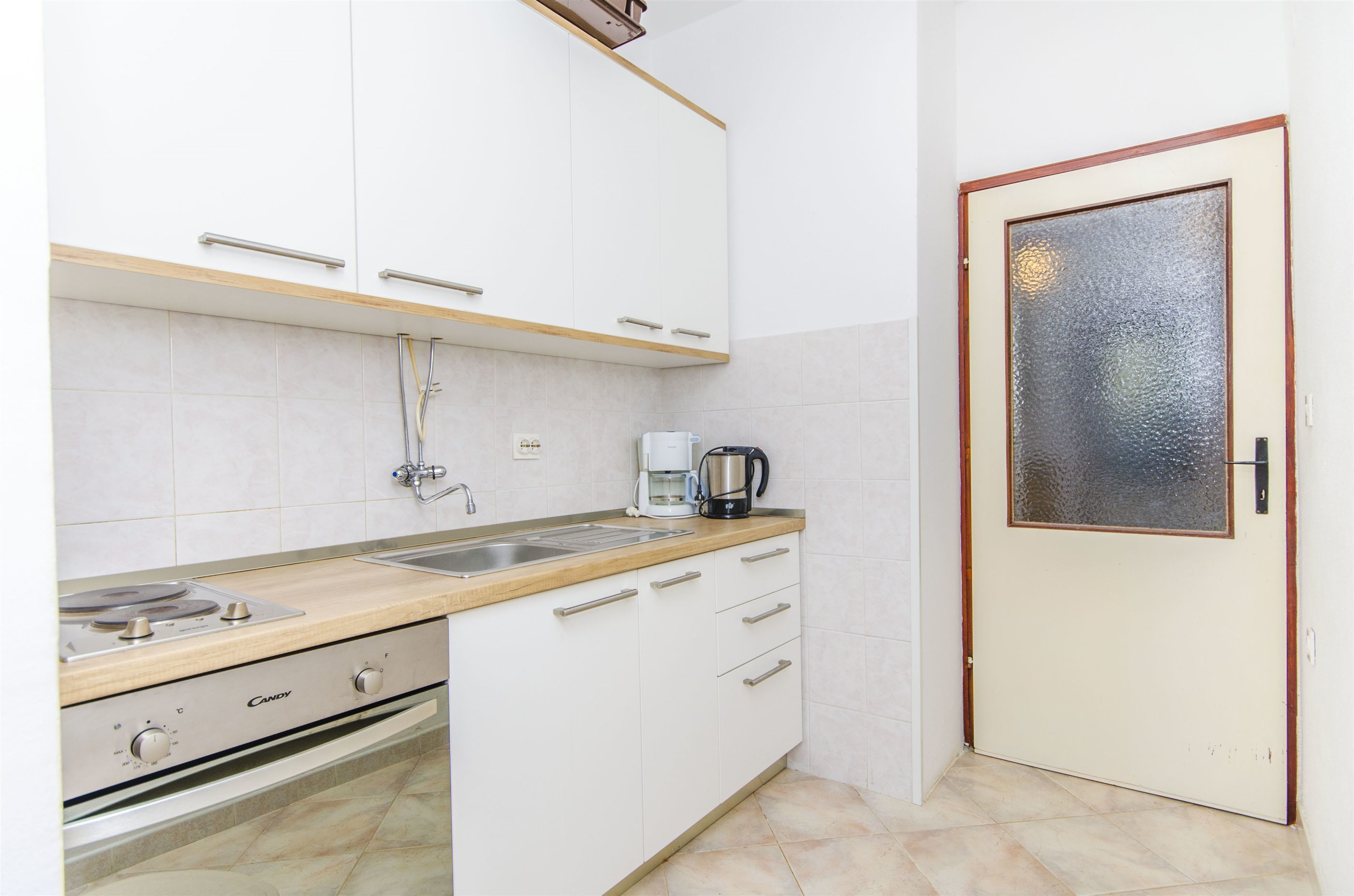 Una cocina con armarios blancos, una encimera, una estufa, un fregadero y una puerta con panel de vidrio esmerilado.