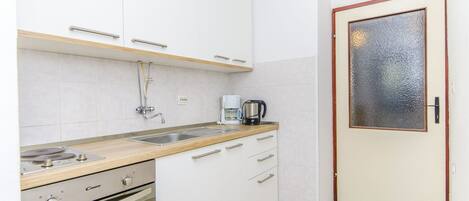 Una cucina con mobili bianchi, un piano di lavoro, un fornello, un lavello e una porta con vetri satinati.