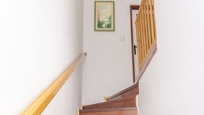 Eine Holztreppe mit Handlauf, die zu einer Tür mit einem Hollgitter führt.