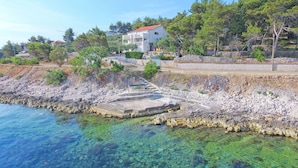 Ein Küstenanwesen mit freiem Blick auf das Meer, ein Steinweg, der zu einem Gebäude führt, und umliegendes Grün.