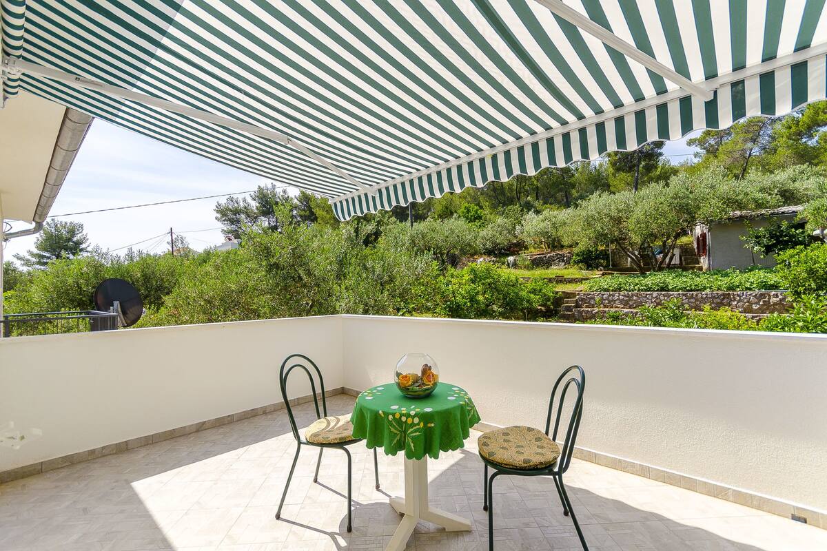 Una terrazza con tavolo e sedie, una tovaglia verde e una ciotola di frutta.