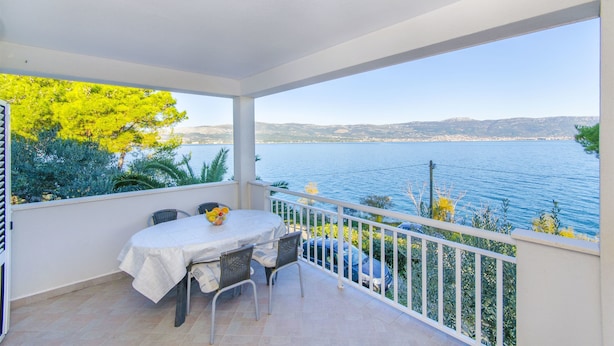 Ein Balkon mit Tisch und Stühlen, der auf ein Gewässer und entfernte Landschaft blickt.
