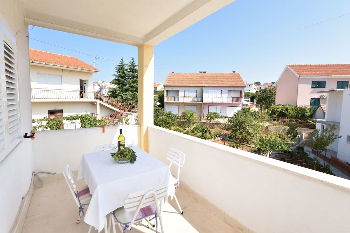 A balcony with a table set for two, a bottle of wine, and a bowl of grapes.
