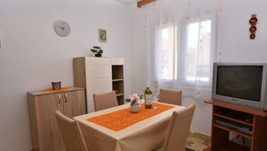 Un coin repas avec une table dressée pour deux personnes, un téléviseur posé sur un meuble en bois et un buffet sur lequel se trouve une plante.