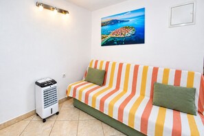 A room with a striped sofa, a standing heater, and a painting of a coastal scene. - Apartment Anka (Primosten)