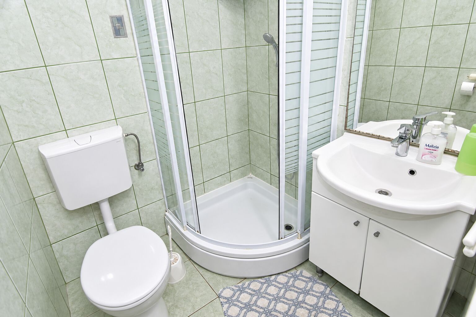 Un baño con inodoro, cabina de ducha y lavabo con artículos de aseo.