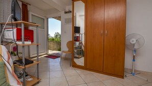 A room with a wooden wardrobe, a TV on a shelf, a fan, and a chair. - Apartment Anka (Primosten)