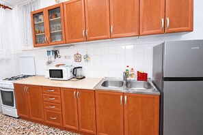 A kitchen with wooden cabinets, a microwave, a gas stove, a refrigerator, and a sink. - Apartment Anka (Primosten)