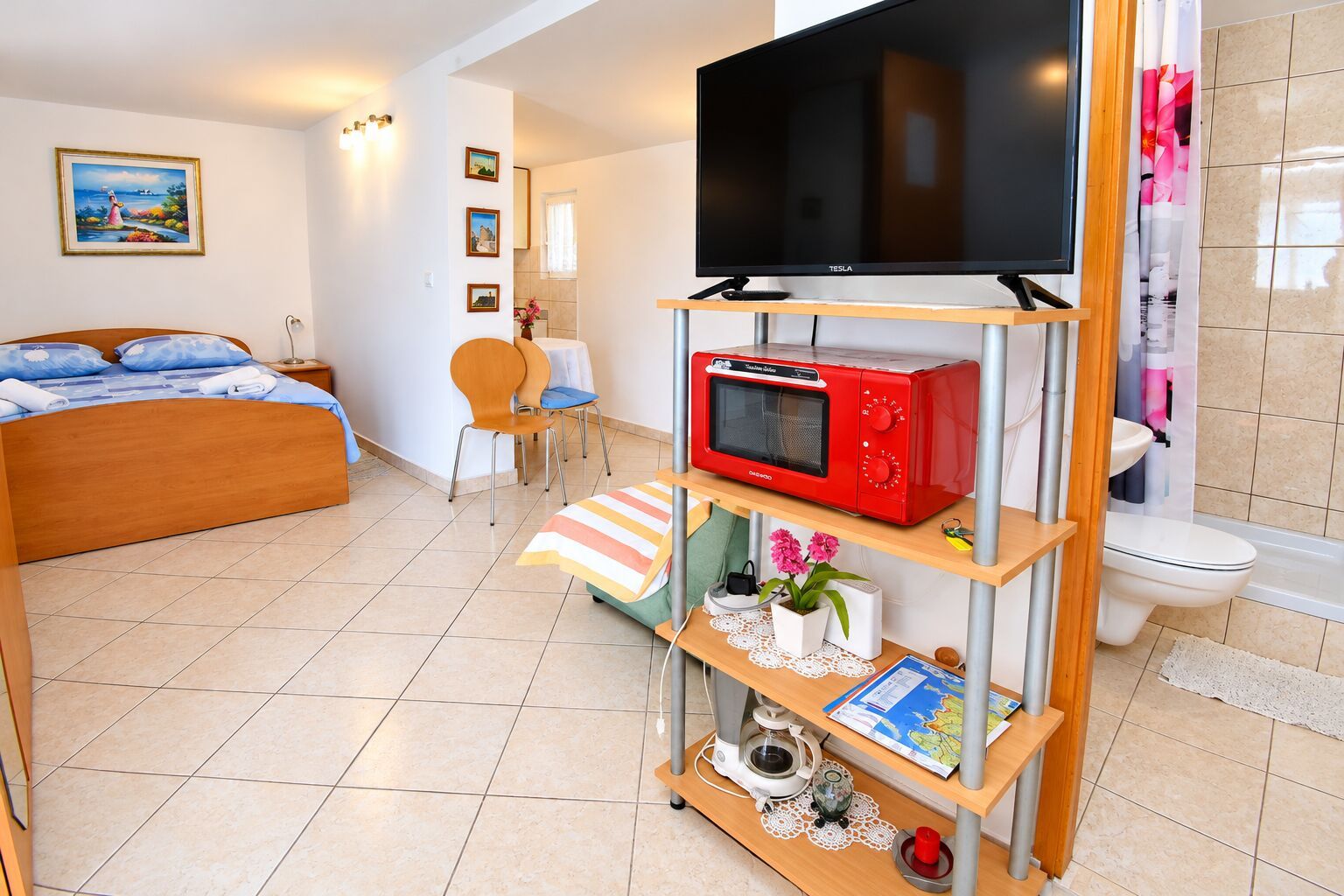 A hotel room with a bed, a TV, a microwave, a small table with a map, and a bathroom with a toilet.