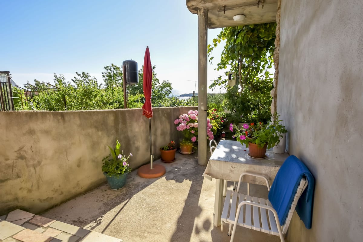 A small outdoor patio with a table and chairs, surrounded by potted plants and a red umbrella.