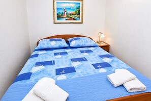 A neatly made bed with a blue and white patterned bedspread, two pillows, and two folded white towels. - Apartment Anka (Primosten)