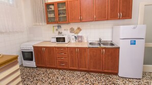 A kitchen with wooden cabinets, a white refrigerator, a microwave, an oven, and a granite countertop. - Apartment Anka (Primosten)