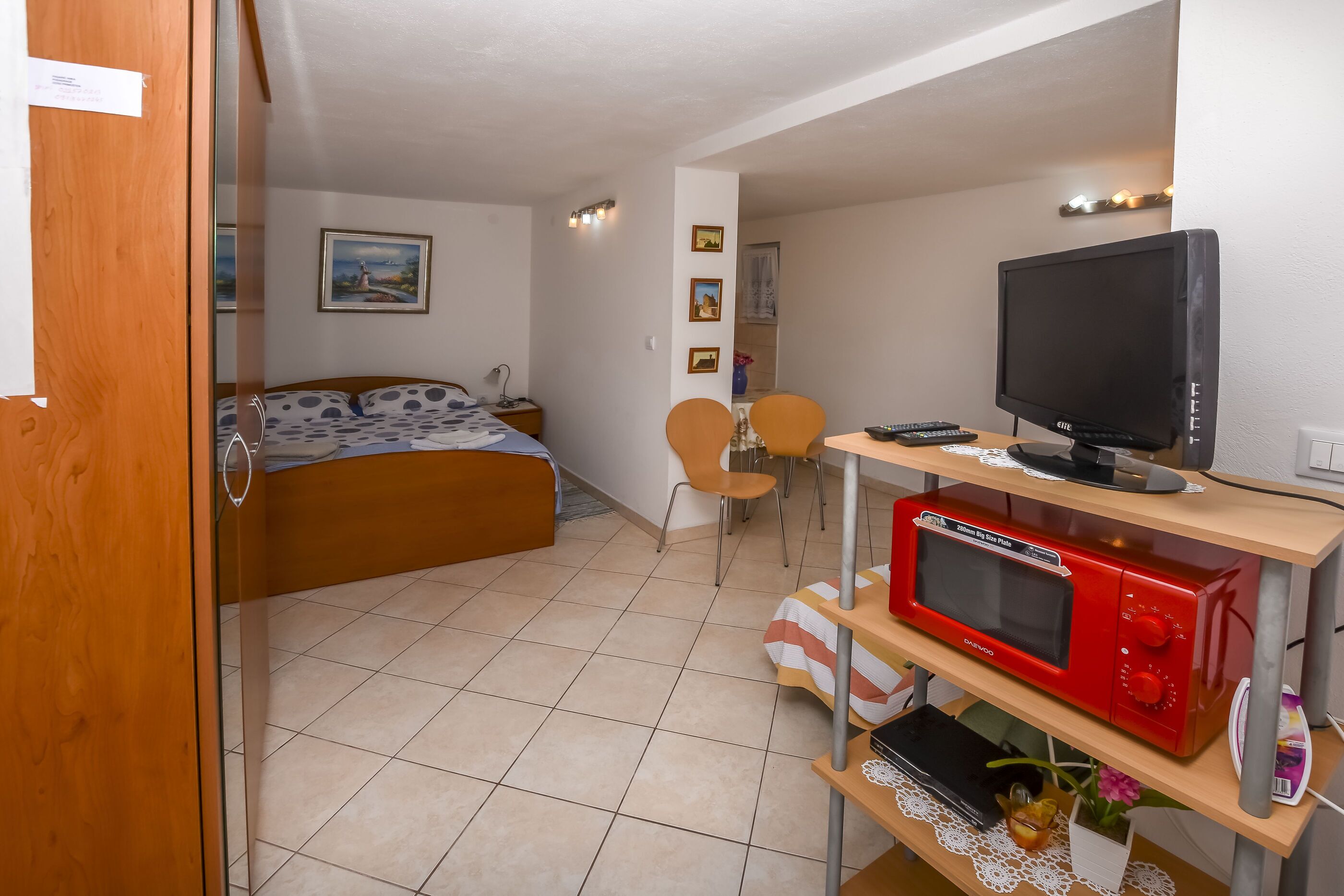Un dormitorio compacto con cama, escritorio con televisor y microondas, y una silla.