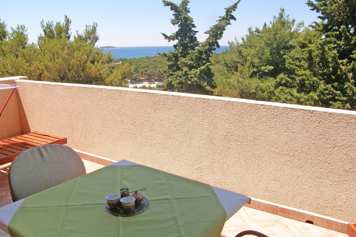 Una terraza con una mesa para dos, una silla y vistas al mar y árboles.