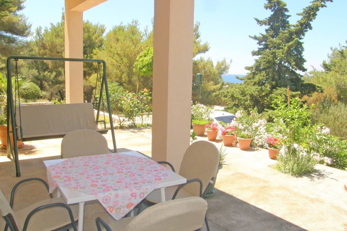 Un patio exterior con una mesa y sillas, rodeado de macetas con plantas y árboles.