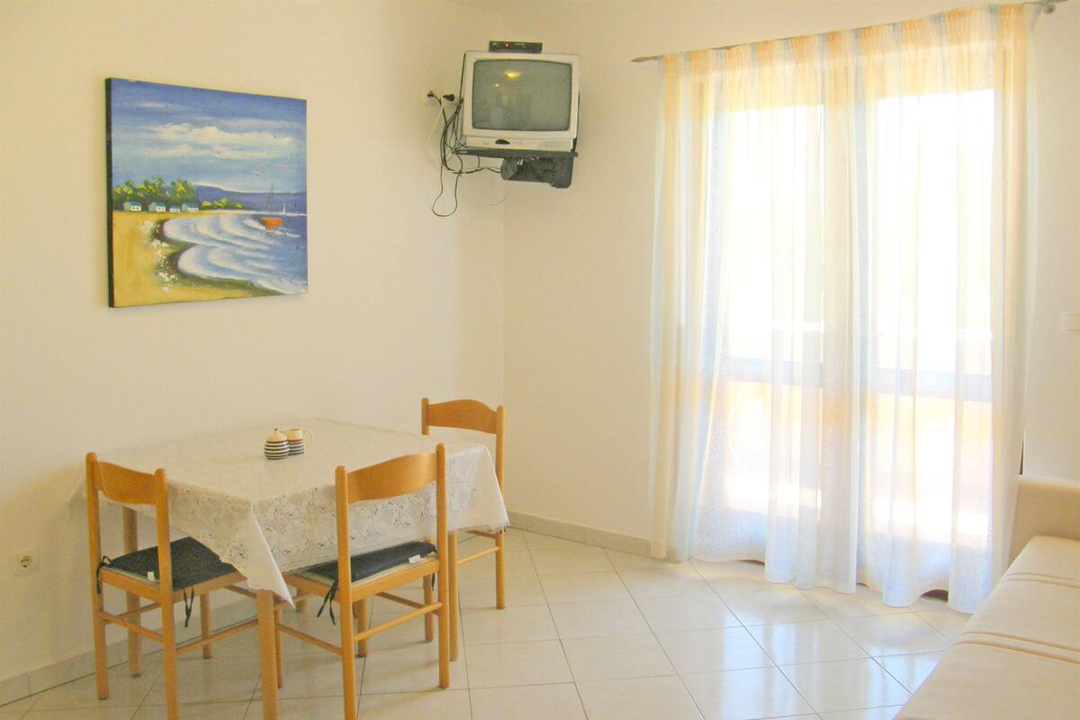 Un comedor con una mesa, sillas, un cuadro, un televisor y una ventana con cortinas.