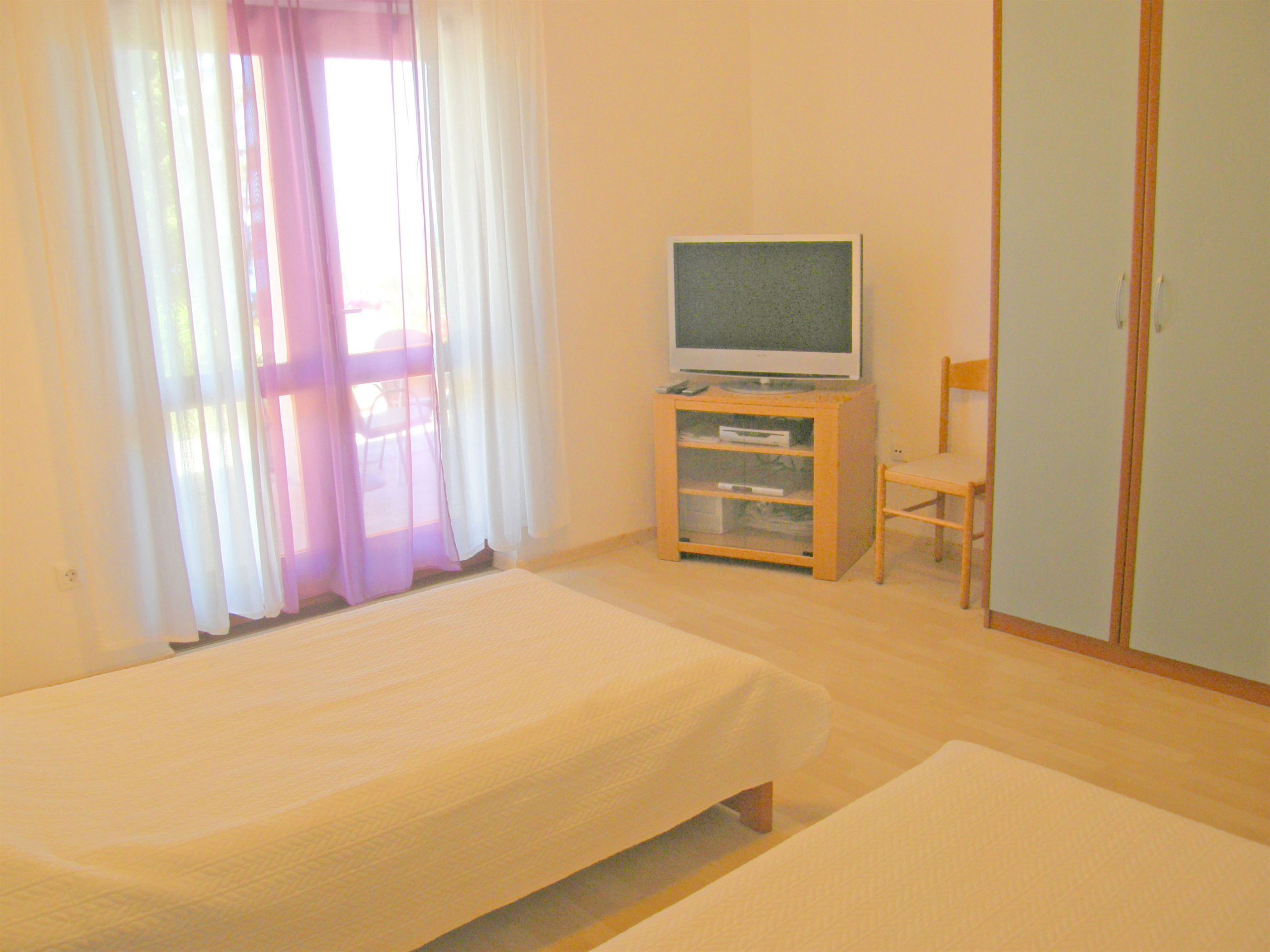 A room with two beds, a television on a wooden stand, and a chair.