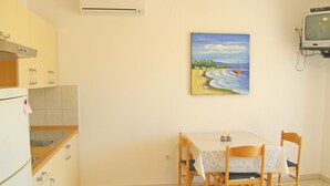 Una pequeña cocina con una mesa de comedor y sillas, un cuadro en la pared y un televisor montado.