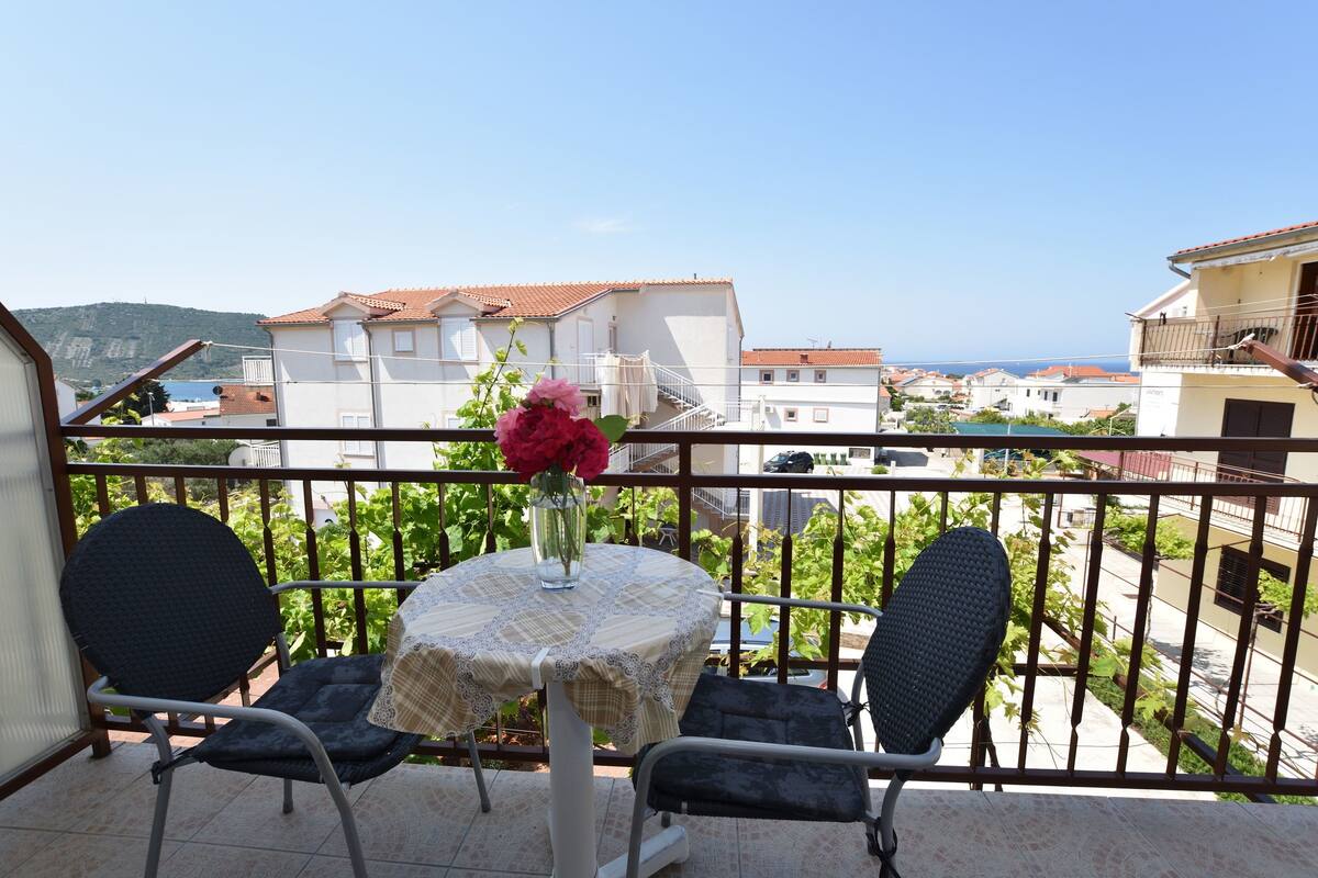 A balcony with two chairs, a table with a lace tablecloth, and a vase with flowers.