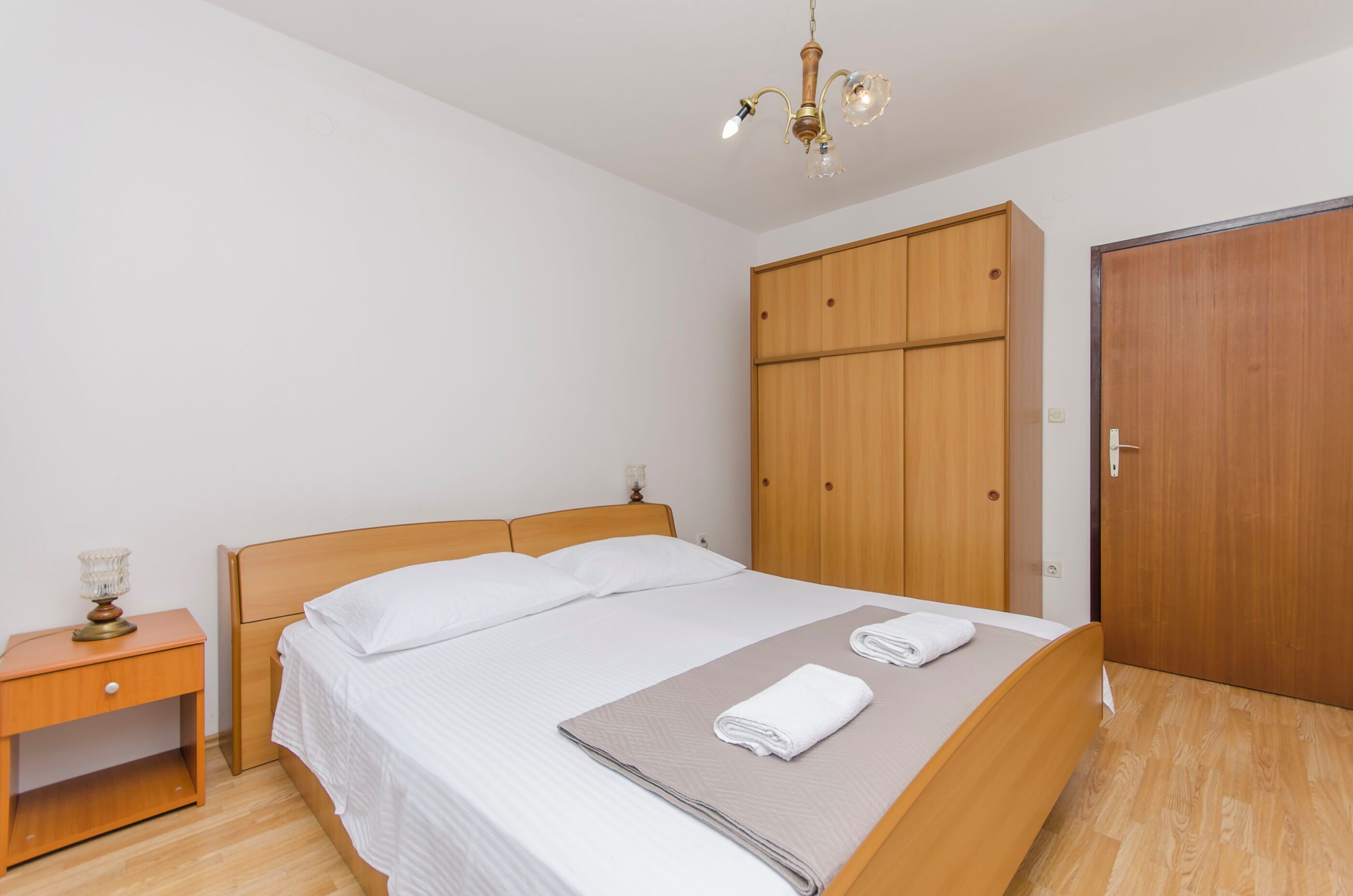 Ein Schlafzimmer mit einem hölzernen Bett, einem Nachttisch, einem Kleiderschrank und einer Kandelaberleuchte.