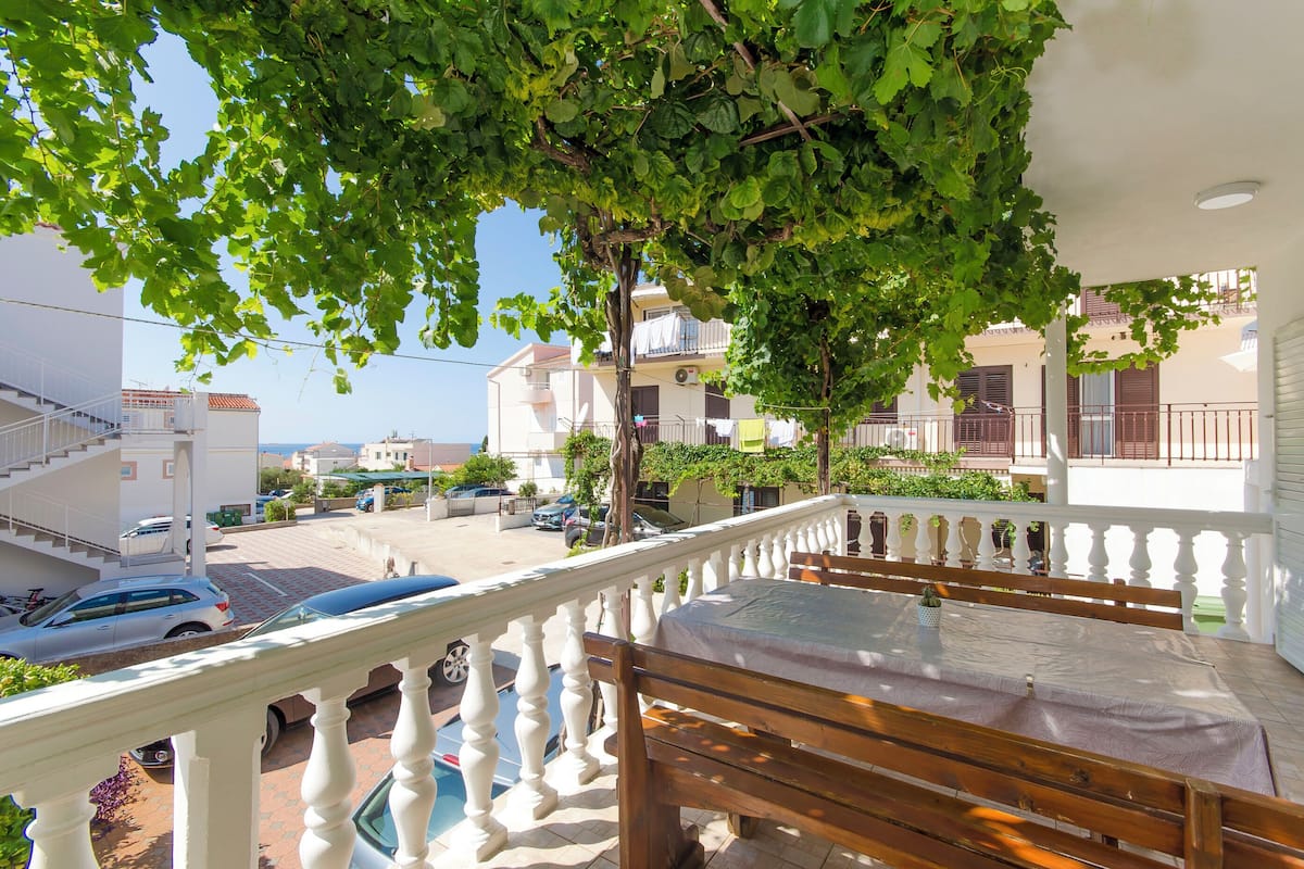 A balcony with a white balustrade, a wooden table, and a view of the street and buildings.