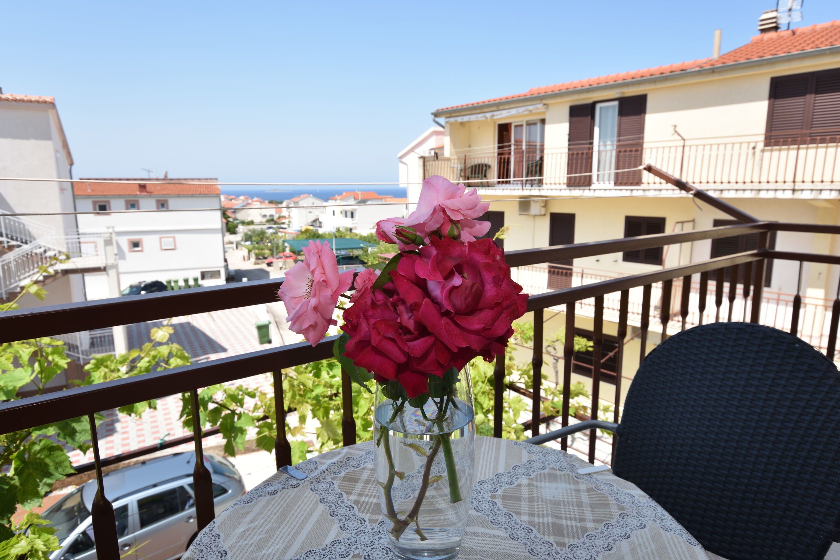 Un balcon avec une table dressée pour deux personnes, donnant sur un quartier résidentiel et la mer.