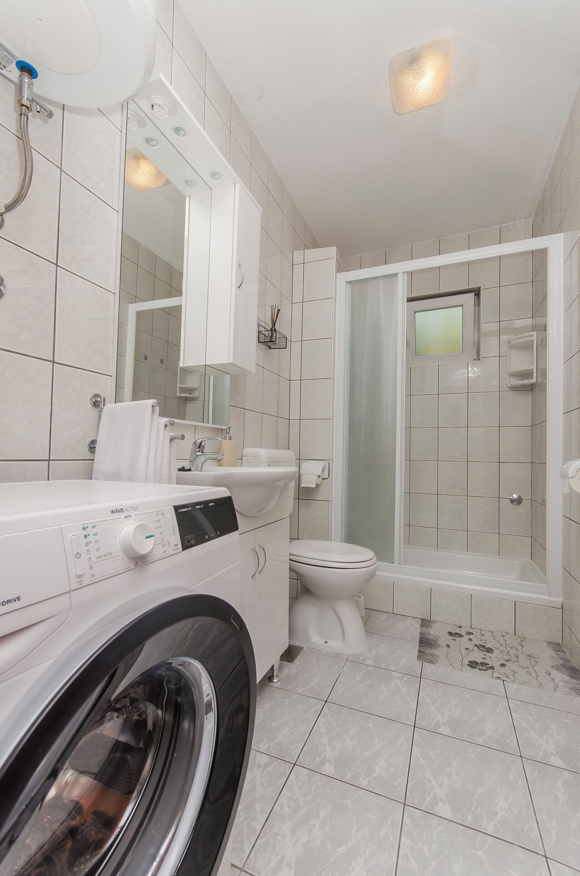 A modern bathroom with a washing machine, toilet, sink, and glass shower enclosure.