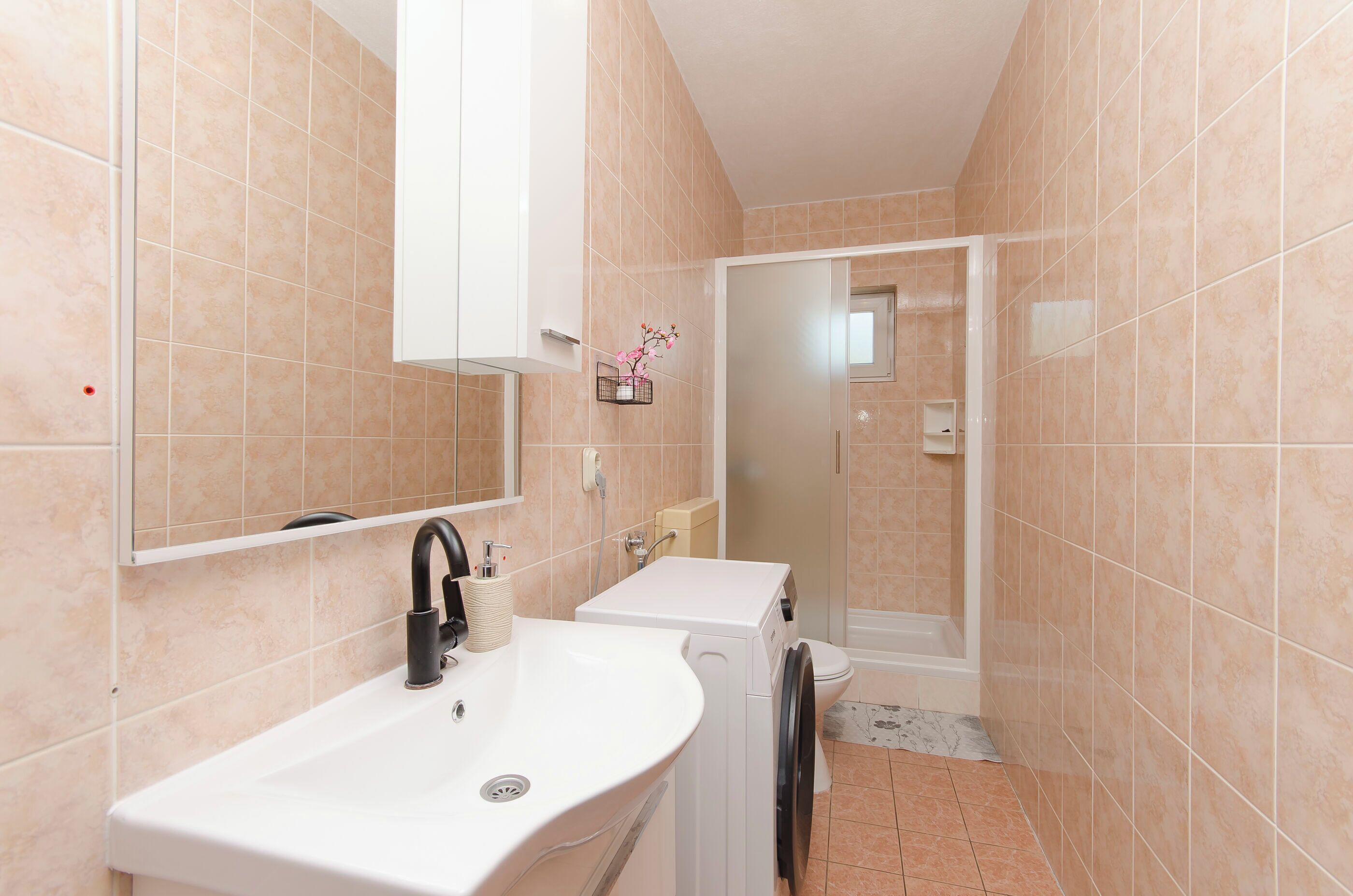 Un baño con lavamanos blanco, un espejo, inodoro y zona de ducha.