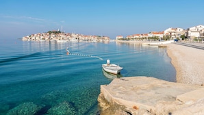 A coastal town with clear waters, a boat docked near the shore, and buildings along the coastline. - Apartment Slavko (Primosten)
